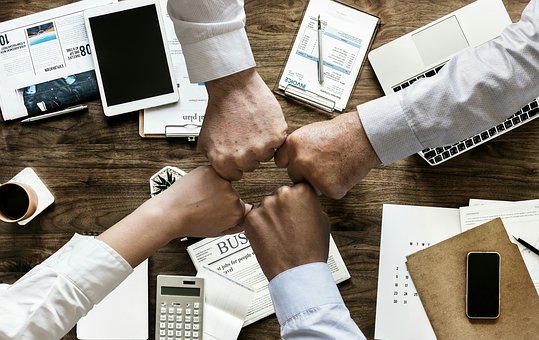 A team of people bring their hands together over a worktable, signifying a successful completion of the project at hand.